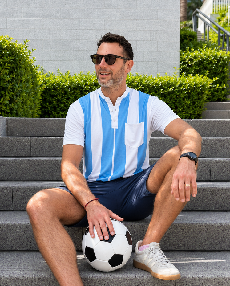 Man sitting on steps holding a soccer ball, wearing a striped shirt and sunglasses.
