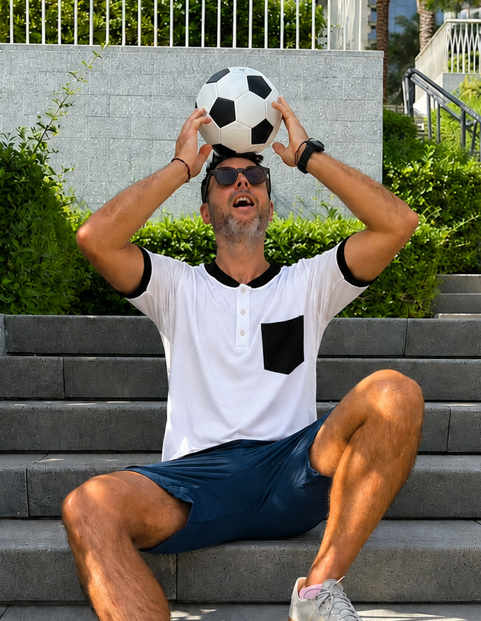 Man sitting on steps holding a soccer ball above his head with a cityscape background