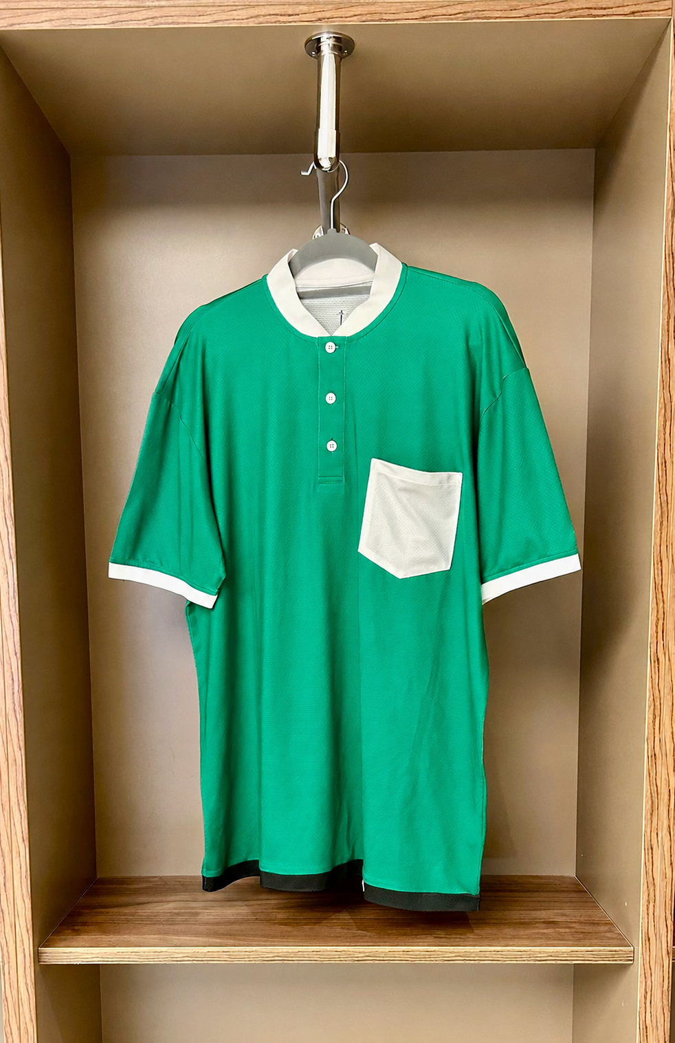 Green shirt with white trim hanging in a wooden shelf