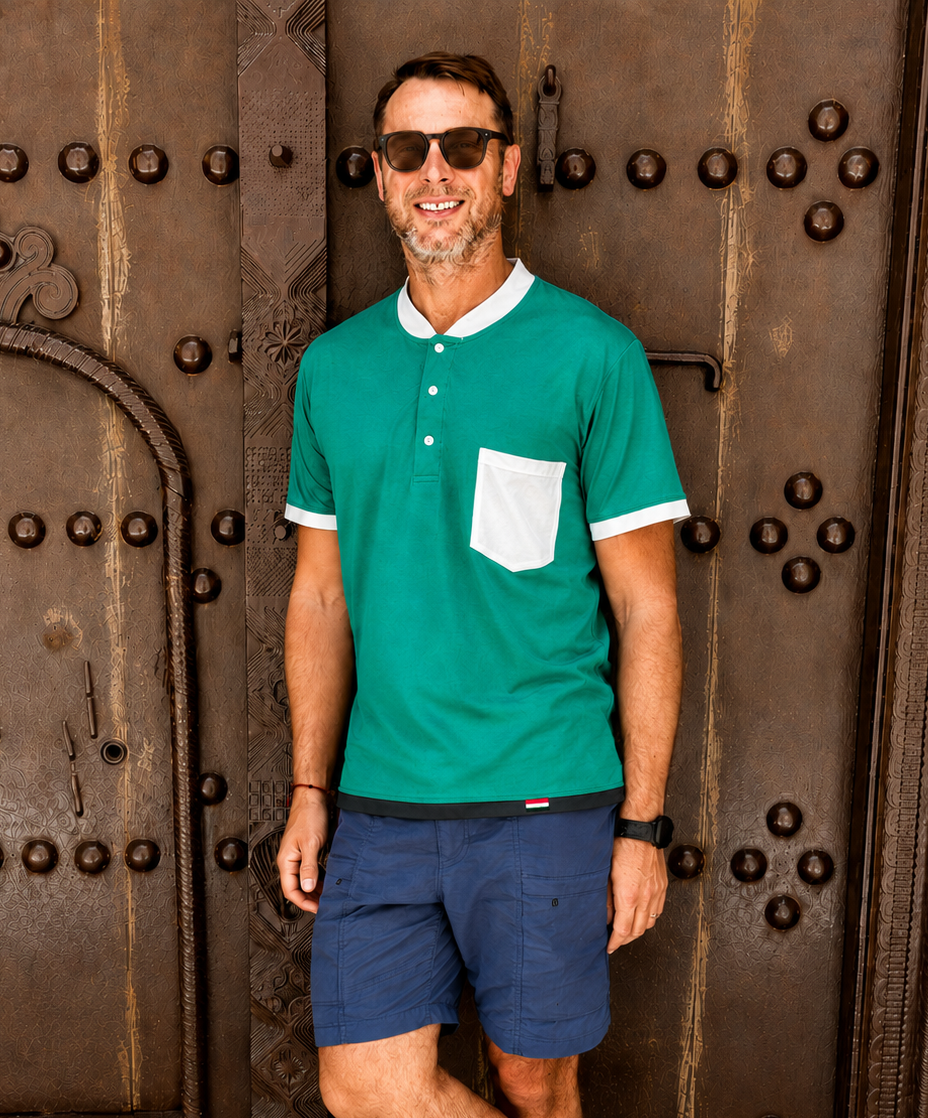 Man wearing a green polo shirt and blue shorts standing in front of a large ornate door.