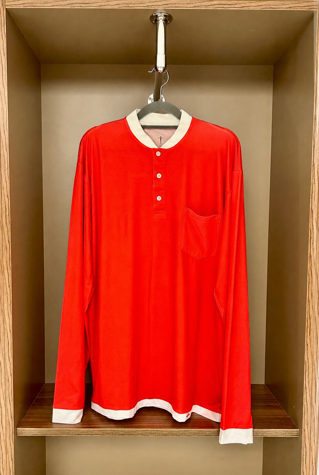 Red long-sleeve shirt with white trim hanging in a wooden shelf.