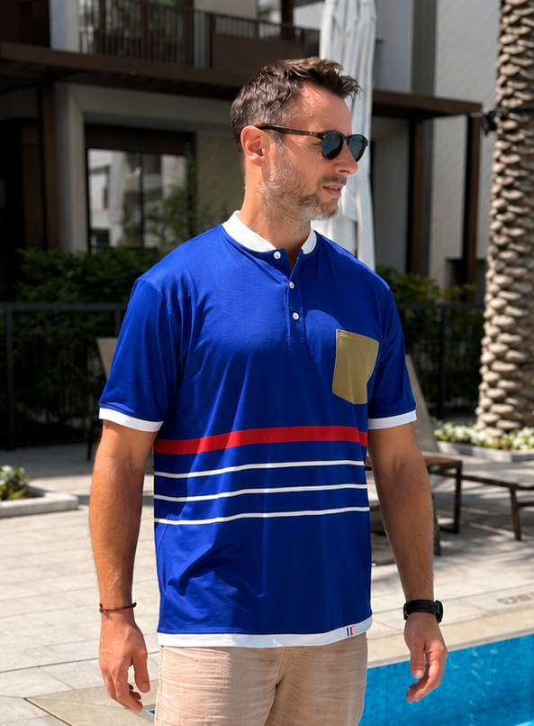 Man in a blue polo shirt and beige shorts standing by a poolside.