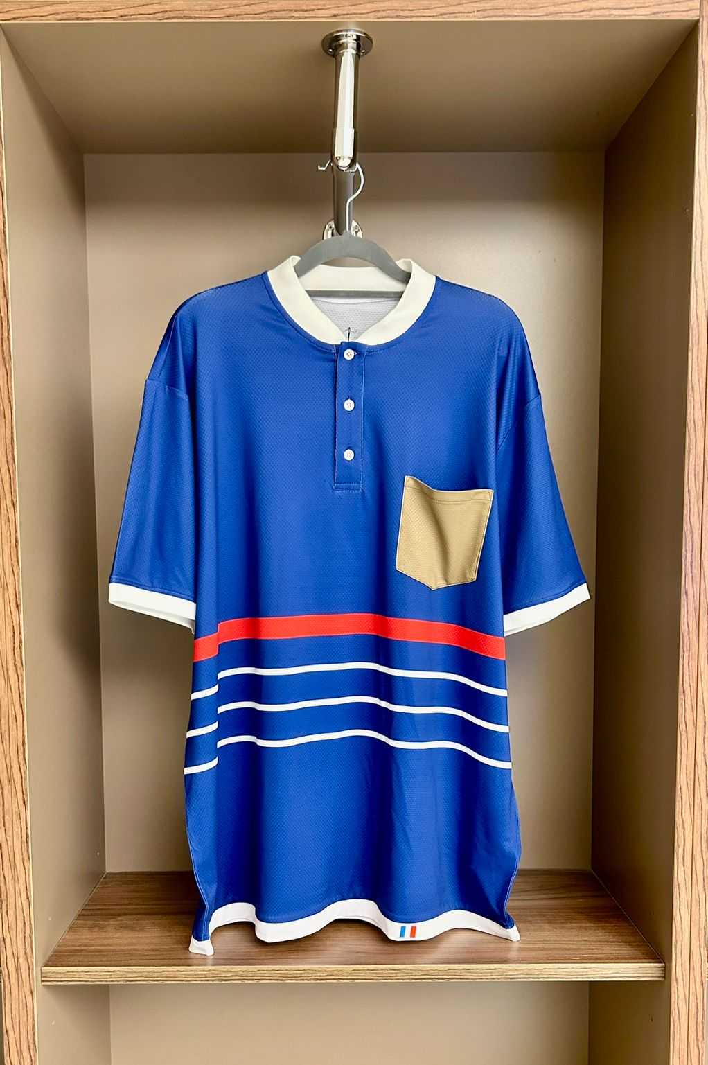 Blue sports jersey with white and red accents hanging in a wooden wardrobe.