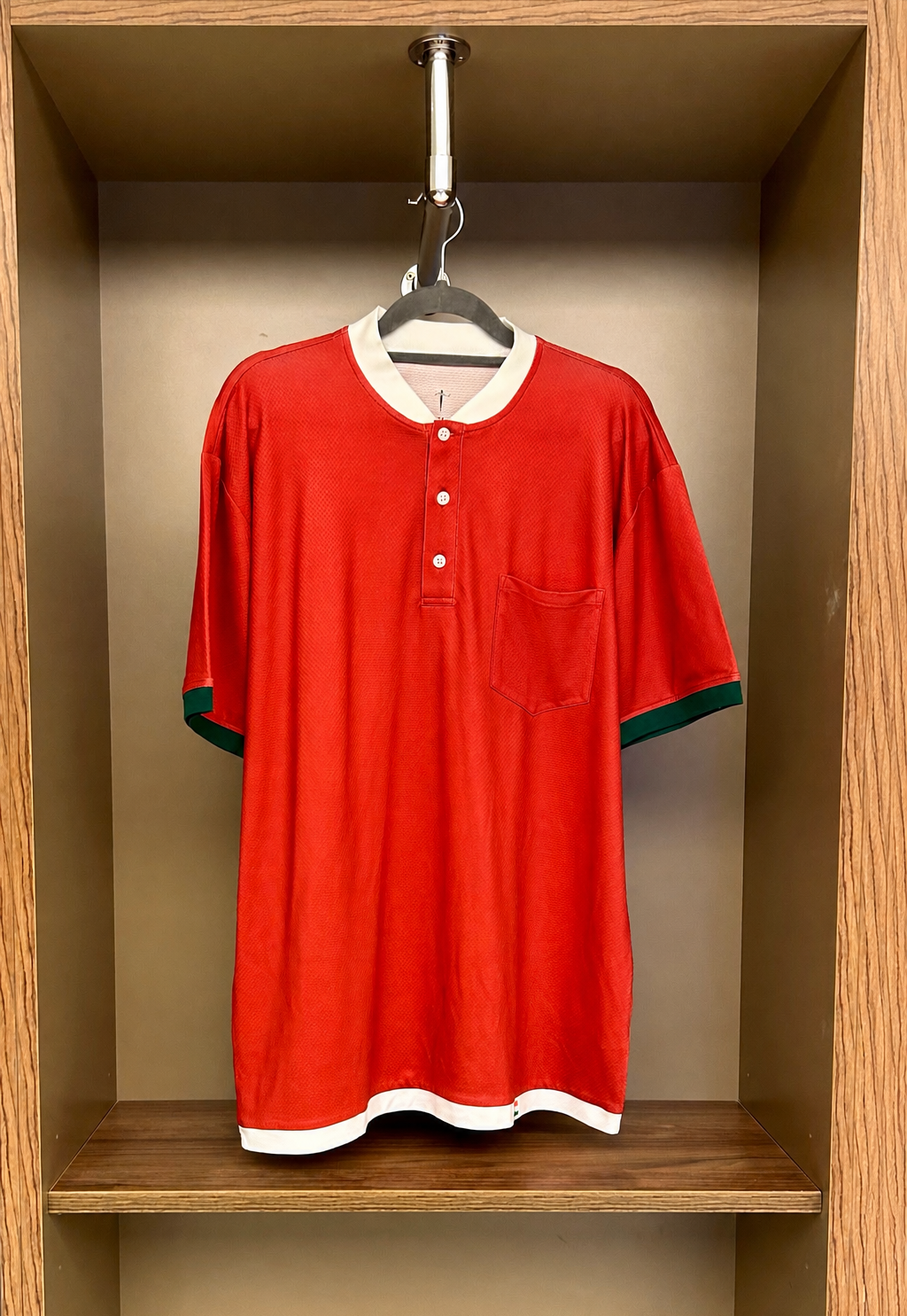 Red shirt with white collar and green trim hanging in a wooden shelf.