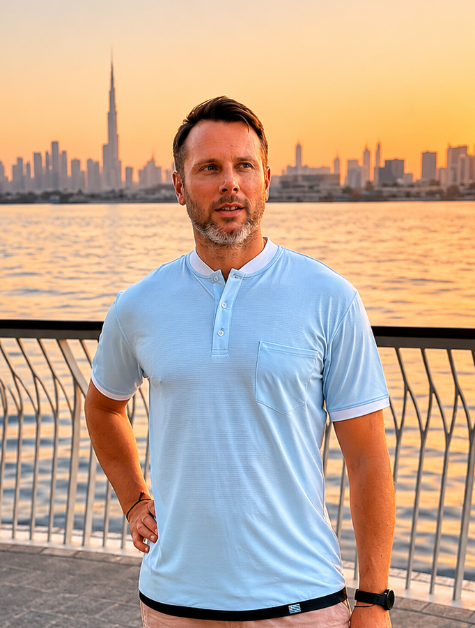 Man standing by a waterfront with a city skyline in the background during sunset.