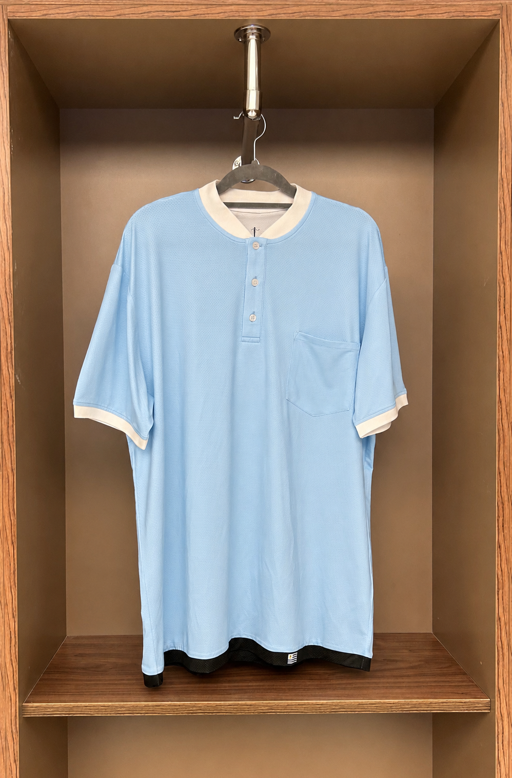Light blue shirt with white trim hanging in a wooden wardrobe.